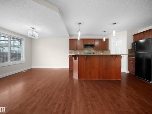 Open concept living space featuring hardwood floors, a kitchen with wood cabinetry and a breakfast bar, and a large window with blinds - 8361 Shaske Crescent, Edmonton, AB - Indoor Photo Showing Kitchen
