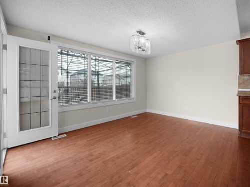 This bright room features hardwood flooring, a modern chandelier, and large windows with horizontal blinds for natural light - 8361 Shaske Crescent, Edmonton, AB - Indoor Photo Showing Other Room