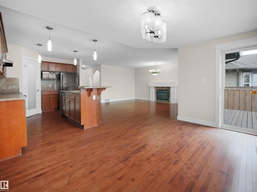 The property features hardwood floors, a kitchen with rich wood cabinetry and stainless steel appliances, and a living area with a fireplace - 8361 Shaske Crescent, Edmonton, AB - Indoor Photo Showing Kitchen With Fireplace