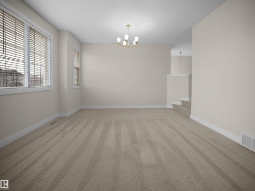 A spacious room featuring neutral-toned walls, plush carpet, and a chandelier, providing a bright and inviting atmosphere - 8361 Shaske Crescent, Edmonton, AB - Indoor Photo Showing Other Room