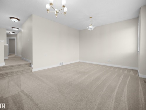 Spacious room featuring neutral carpeting, light-colored walls, and a decorative chandelier, with a view towards a hallway with recessed lighting - 8361 Shaske Crescent, Edmonton, AB - Indoor Photo Showing Other Room