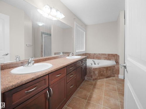The bathroom features a double vanity with ample storage, a large mirror, and an integrated corner bathtub with tiled surround - 8361 Shaske Crescent, Edmonton, AB - Indoor Photo Showing Bathroom