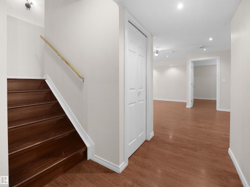 The property features a staircase with dark wood treads and a light-colored wooden handrail, complemented by white baseboards - 8361 Shaske Crescent, Edmonton, AB - Indoor Photo Showing Other Room