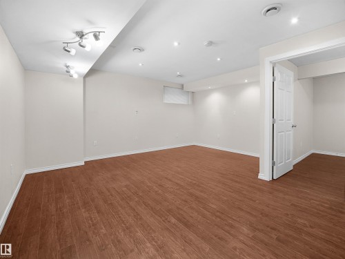 Spacious room featuring wood-look flooring, light-colored walls, recessed lighting, and a white interior door - 8361 Shaske Crescent, Edmonton, AB - Indoor Photo Showing Other Room