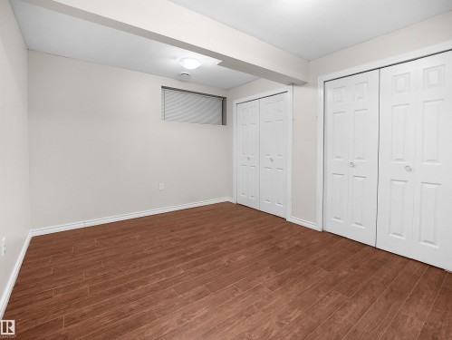 This versatile room features wood-look flooring, light-colored walls, and two sets of bi-fold closet doors, offering ample storage - 8361 Shaske Crescent, Edmonton, AB - Indoor Photo Showing Other Room
