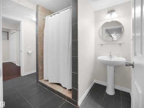 The bathroom features dark tiled flooring, a shower with tiled walls and a shower curtain, and a pedestal sink with a mirror - 8361 Shaske Crescent, Edmonton, AB - Indoor Photo Showing Bathroom