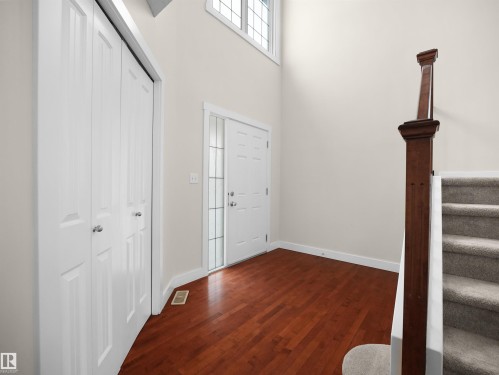 Inviting entryway featuring rich hardwood flooring, a white front door with decorative glass panels, and a staircase with a dark wood newel post and carpeted steps - 8361 Shaske Crescent, Edmonton, AB - Indoor Photo Showing Other Room