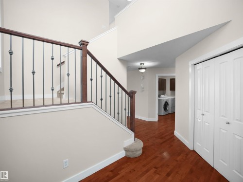 The property features a staircase with a wooden handrail and decorative metal balusters, along with hardwood flooring in the hallway - 8361 Shaske Crescent, Edmonton, AB - Indoor Photo Showing Other Room