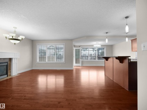 This spacious living area features polished hardwood flooring, a fireplace with a white mantel, and a large window providing natural light - 8361 Shaske Crescent, Edmonton, AB - Indoor Photo Showing Living Room With Fireplace