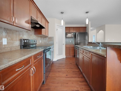 The kitchen features wood cabinetry, a tiled backsplash, and stainless steel appliances including a refrigerator, stove, and dishwasher - 8361 Shaske Crescent, Edmonton, AB - Indoor Photo Showing Kitchen With Double Sink