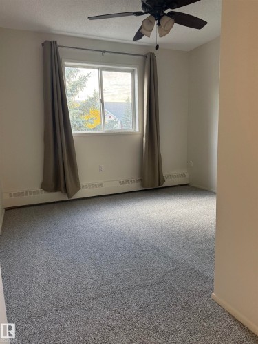 This room features a window with curtains, a ceiling fan, and carpeted flooring - 331 10636 120 Street, Edmonton, AB - Indoor