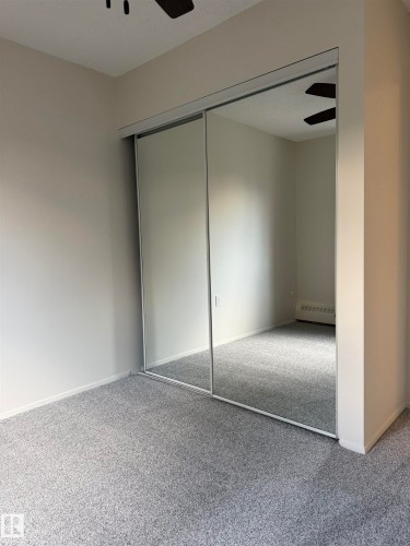 Room featuring a ceiling fan, light gray carpeting, and mirrored closet doors - 331 10636 120 Street, Edmonton, AB - Indoor Photo Showing Other Room