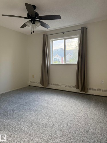 This room features neutral-toned carpet, a window with curtains, and a ceiling fan with integrated lighting - 331 10636 120 Street, Edmonton, AB - Indoor Photo Showing Other Room