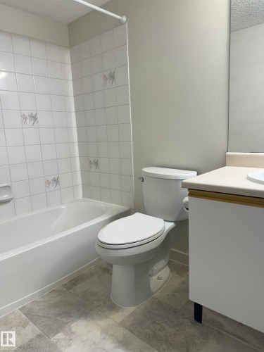 Bathroom featuring a white bathtub with tiled walls, a white toilet, and a vanity with a light-colored countertop - 331 10636 120 Street, Edmonton, AB - Indoor Photo Showing Bathroom