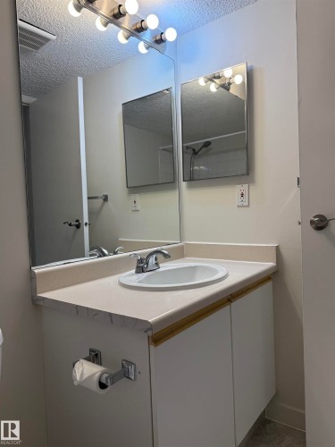 Bathroom vanity featuring a countertop with an integrated sink, a chrome faucet, and a large mirror - 331 10636 120 Street, Edmonton, AB - Indoor Photo Showing Bathroom