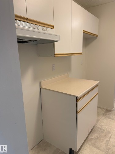 Kitchen featuring white cabinetry with gold-toned trim, a light-colored countertop, and a range hood - 331 10636 120 Street, Edmonton, AB - Indoor