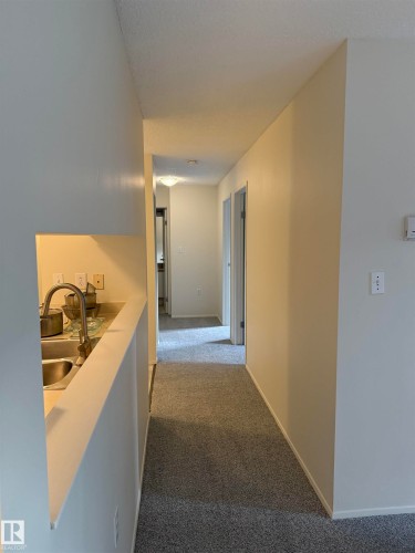 The property features a hallway with carpeted flooring and light-colored walls - 331 10636 120 Street, Edmonton, AB - Indoor