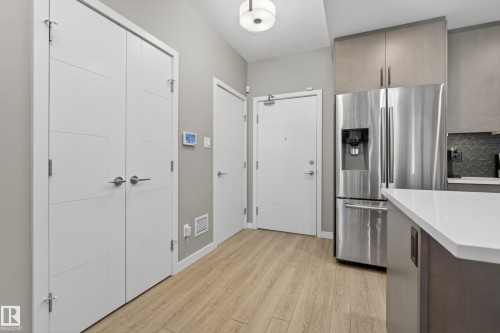 The property features light-colored wood flooring, a stainless steel refrigerator, and modern white doors - 127 1154 Adamson Drive, Edmonton, AB - Indoor