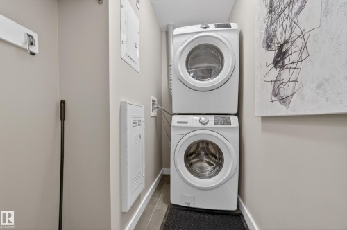 Dedicated laundry space featuring a stackable washer and dryer, tile flooring, and light-colored walls - 127 1154 Adamson Drive, Edmonton, AB - Indoor Photo Showing Laundry Room