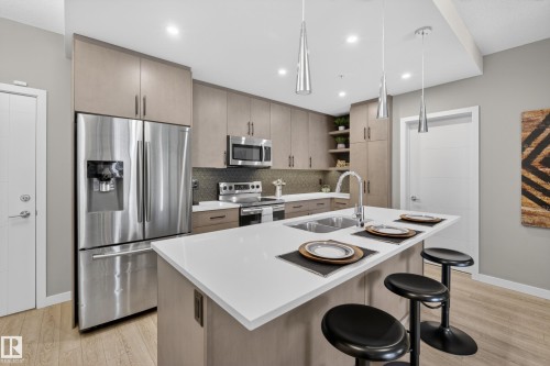 The kitchen features stainless steel appliances, contemporary cabinetry, a kitchen island with a double sink, and sleek pendant lighting - 127 1154 Adamson Drive, Edmonton, AB - Indoor Photo Showing Kitchen With Stainless Steel Kitchen With Double Sink With Upgraded Kitchen