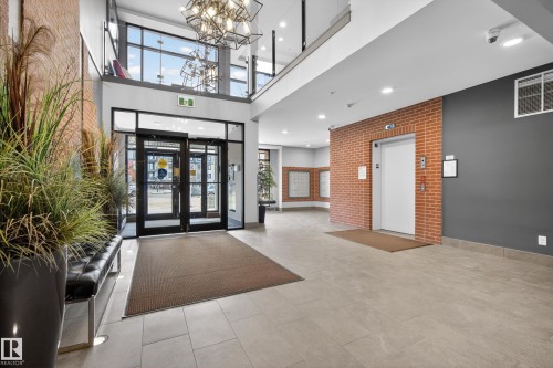 The property features a spacious lobby with brick accent walls, a large modern chandelier, and an elevator - 127 1154 Adamson Drive, Edmonton, AB - Indoor Photo Showing Other Room