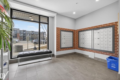 The property features a lobby area with a large window, tiled flooring, and accent brick walls - 127 1154 Adamson Drive, Edmonton, AB - Indoor Photo Showing Other Room