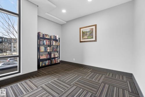 This room features a floor-to-ceiling window, a bookshelf filled with books, and patterned carpet flooring - 127 1154 Adamson Drive, Edmonton, AB - Indoor Photo Showing Other Room