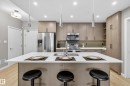 The kitchen features a spacious island with a white countertop and seating, stainless steel appliances, and extensive cabinetry for storage - 127 1154 Adamson Drive, Edmonton, AB  - Indoor Photo Showing Kitchen With Stainless Steel Kitchen With Upgraded Kitchen 