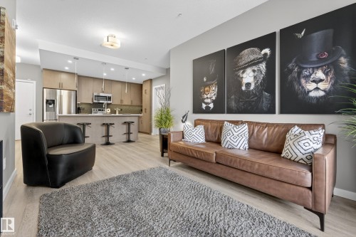 The open concept living area features light-toned flooring, a kitchen with stainless steel appliances, and sleek overhead lighting - 127 1154 Adamson Drive, Edmonton, AB - Indoor Photo Showing Living Room
