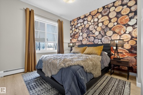Bedroom featuring light wood flooring, a window providing natural light, and a striking accent wall with a wood log design - 127 1154 Adamson Drive, Edmonton, AB - Indoor Photo Showing Bedroom