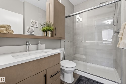Bathroom featuring a contemporary vanity with a white countertop and chrome faucet, a large mirror, and a glass-enclosed shower with subway tile - 127 1154 Adamson Drive, Edmonton, AB - Indoor Photo Showing Bathroom