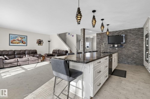 Open concept living area featuring a kitchen island with dark countertops, white cabinetry, and a stainless steel sink - 19 Escada Close, St. Albert, AB - Indoor