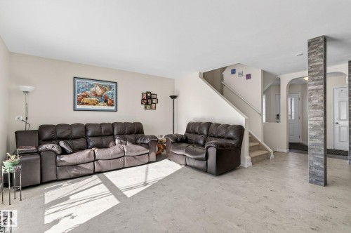 Spacious living area featuring light-colored flooring, a staircase with carpeted treads, and an arched doorway - 19 Escada Close, St. Albert, AB - Indoor Photo Showing Living Room
