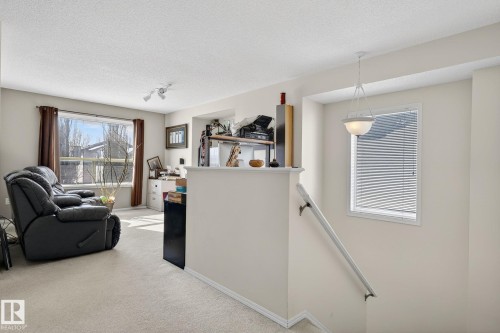 This inviting interior features light-colored walls and carpeting, a window with brown curtains, and a prominent light fixture - 19 Escada Close, St. Albert, AB - Indoor