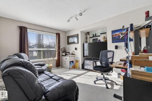 The room features carpeted flooring, a large window with brown curtains, and a built-in shelving unit - 19 Escada Close, St. Albert, AB - Indoor