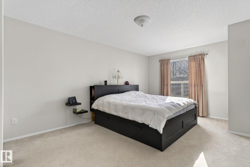 This bedroom features light-colored walls and carpeting, a window with curtains, and a ceiling light fixture - 19 Escada Close, St. Albert, AB - Indoor Photo Showing Bedroom