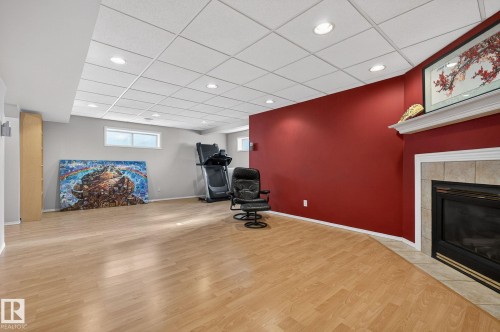 The property features a spacious room with light wood-style flooring, a fireplace with a tiled surround, and recessed lighting - 19 Escada Close, St. Albert, AB - Indoor With Fireplace