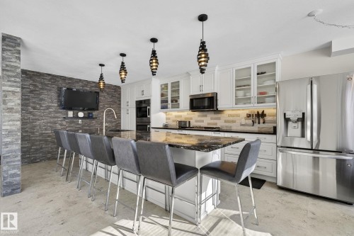 The kitchen features white cabinetry, stainless steel appliances, and a central island with a dark countertop and seating - 19 Escada Close, St. Albert, AB - Indoor
