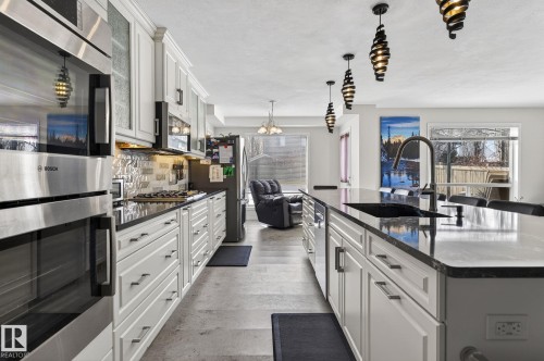 The kitchen features white cabinetry, dark countertops, a built-in oven, and a large island with a sink - 19 Escada Close, St. Albert, AB - Indoor Photo Showing Kitchen With Upgraded Kitchen