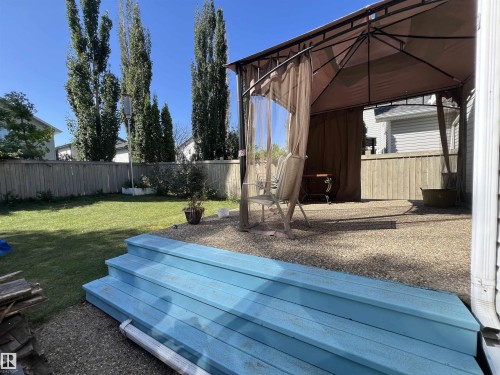 The property includes a spacious yard featuring a lawn, mature trees, and a wooden fence - 19 Escada Close, St. Albert, AB - Outdoor