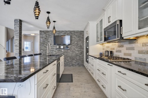 The kitchen features a large island with a dark granite countertop, white cabinetry with dark hardware, and a gas range - 19 Escada Close, St. Albert, AB - Indoor Photo Showing Kitchen With Upgraded Kitchen