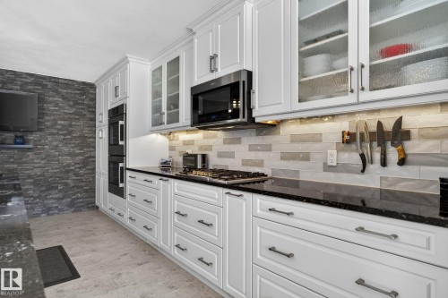 The kitchen features white cabinetry with dark hardware, black granite countertops, a gas cooktop, and built-in double ovens - 19 Escada Close, St. Albert, AB - Indoor Photo Showing Kitchen With Upgraded Kitchen
