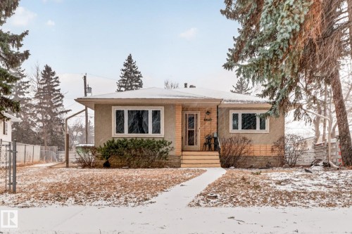 The property features a stucco exterior, a pathway leading to the front entrance, and a front yard with mature trees - 11255 71 Avenue, Edmonton, AB - Outdoor