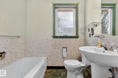 Bathroom featuring a white bathtub, a pedestal sink, and a window with green trim - 11255 71 Avenue, Edmonton, AB - Indoor Photo Showing Bathroom