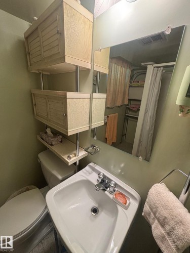 Bathroom featuring a white sink with a chrome faucet, a wall-mounted mirror, and overhead cabinetry providing storage - 11255 71 Avenue, Edmonton, AB - Indoor Photo Showing Bathroom