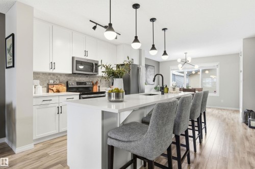 The kitchen features a large island with seating, white cabinetry, a stainless steel microwave, and a black faucet - 3247 Cherry Crescent, Edmonton, AB - Indoor Photo Showing Kitchen With Upgraded Kitchen