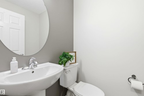 Bathroom featuring a pedestal sink with a chrome faucet, a round mirror, and a toilet - 3247 Cherry Crescent, Edmonton, AB - Indoor Photo Showing Bathroom