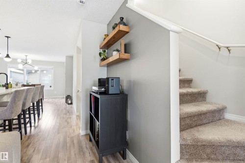 Interior featuring light wood-style flooring, a staircase with carpeted treads, and built-in wooden shelves on a grey wall - 3247 Cherry Crescent, Edmonton, AB - Indoor