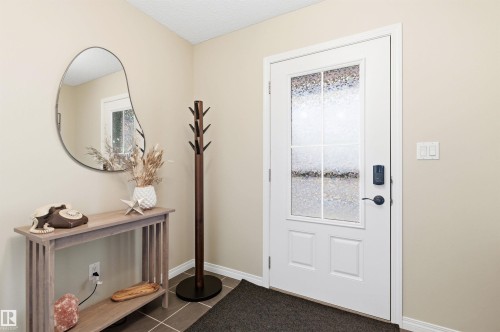 The property features a white front door with frosted glass panels and a digital lock, complemented by a light-colored wall and dark floor tiles - 3247 Cherry Crescent, Edmonton, AB - Indoor Photo Showing Other Room