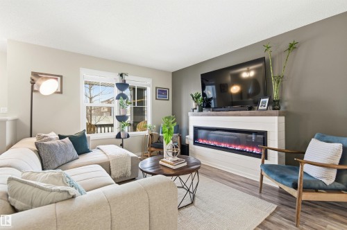 Living area featuring light wood-style flooring, a large window, and a fireplace with a white shiplap-style surround and a dark mantel - 3247 Cherry Crescent, Edmonton, AB - Indoor Photo Showing Living Room With Fireplace